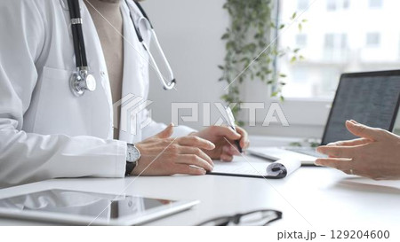 Doctor listening to patient health concerns and writing a prescription during a consultation in a bright, modern clinic. Medicine and health care concept 129204600