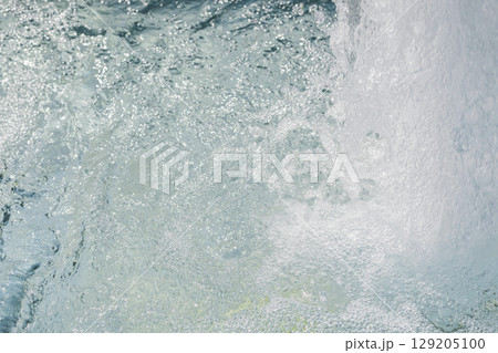 Bubbles rise through crystal clear water from a natural spring, creating a lively atmosphere in a tranquil environment illuminated by bright daylight 129205100