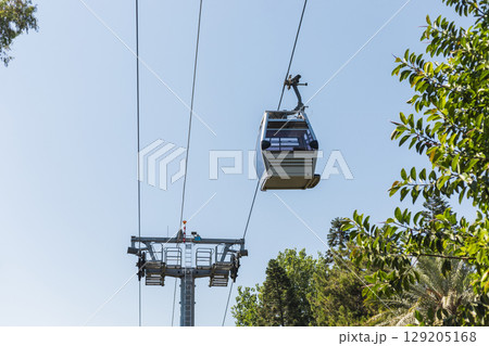 A cable car glides smoothly along overhead cables, offering a breathtaking view of the vibrant green trees below in a serene outdoor environment. It is a sunny day, perfect for exploration A cable car glides smoothly along overhead cables, offering a breathtaking view of the vibrant green trees below in a serene outdoor environment. It is a sunny day, perfect for exploration 129205168