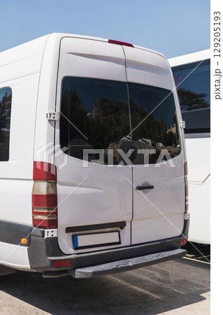 A large white van with tinted windows is parked in a transport area beside another vehicle. The clear blue sky enhances the focus on the two vehicles 129205193
