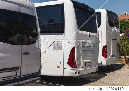 Several white buses are parked closely together at a transportation hub under clear blue skies. The vehicles are in pristine condition, showcasing their sleek designs Several white buses are parked closely together at a transportation hub under clear blue skies. The vehicles are in pristine condition, showcasing their sleek designs 129205194