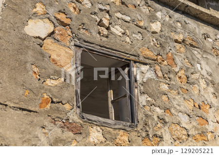 An abandoned structure features a weathered stone wall and a simple wooden window. Sunlight casts warm tones on the rustic texture, highlighting the village's charm An abandoned structure features a weathered stone wall and a simple wooden window. Sunlight casts warm tones on the rustic texture, highlighting the village's charm 129205221