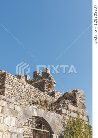 Visitors can admire the weathered stone ruins that tell stories of a bygone era. The structure features remnants of intricate architecture against a vibrant blue sky Visitors can admire the weathered stone ruins that tell stories of a bygone era. The structure features remnants of intricate architecture against a vibrant blue sky 129205237
