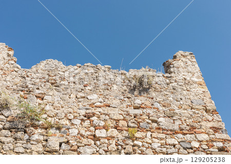 The weathered stone wall stands against a vibrant blue sky, showcasing its historical significance and architectural details. Nature has begun to reclaim parts of this structure 129205238