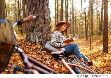 Beautiful young woman sitting on a fallen autumn leaves in a park, reading a book. Beautiful young woman sitting on a fallen autumn leaves in a park, reading a book. 129205667