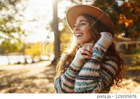 Sunny lifestyle portrait of young stylish woman walking on park, wearing cute trendy hat. Relaxation 129205676