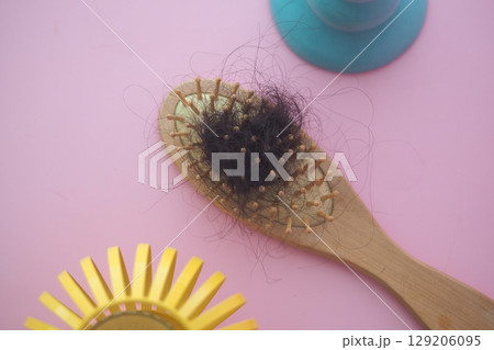 A wooden hairbrush with loose hair on a pink background . A wooden hairbrush with loose hair on a pink background . 129206095