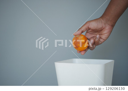 Discarding a spoiled orange in a waste bin Discarding a spoiled orange in a waste bin 129206130
