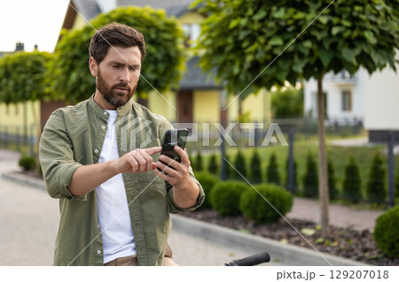 Bearded man on a bike with a phone in hands 129207018