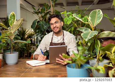 Flower shop assistant analyzing online orders and looking contented Flower shop assistant analyzing online orders and looking contented 129207083