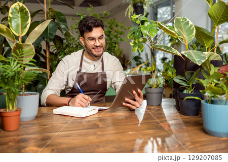 Flower shop assistant analyzing online orders and looking contented 129207085
