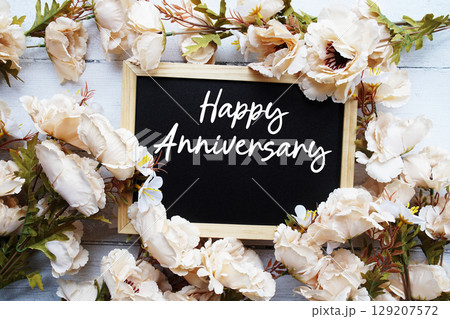Happy Anniversary text with flower decoration on wooden background 129207572