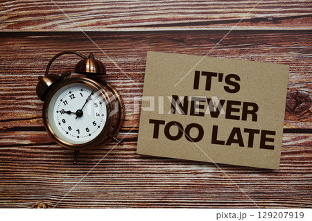 It's Never Too Late text with alarm clock on wooden background 129207919