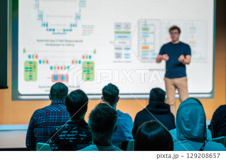 Speaker presenting a technical workshop to an attentive audience with diagrams on screen Speaker presenting a technical workshop to an attentive audience with diagrams on screen 129208657