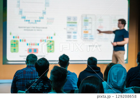 Speaker presenting to audience with detailed schematic displayed on screen 129208658