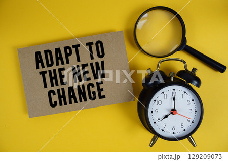 Adapt To The New Change text written on paper with magnifying glass and alarm clock on yellow background 129209073