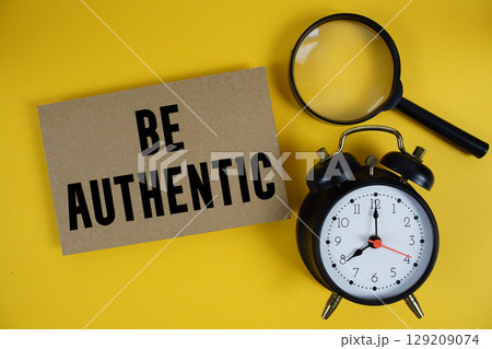 Be Authentic text written on paper with magnifying glass and alarm clock on yellow background Be Authentic text written on paper with magnifying glass and alarm clock on yellow background 129209074