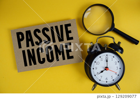 Passive Income text written on paper with magnifying glass and alarm clock on yellow background 129209077