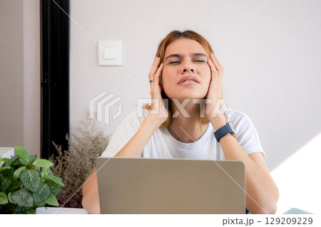 Unhappy young caucasian businesswoman using laptop computer on desk with stress and burnout. 129209229