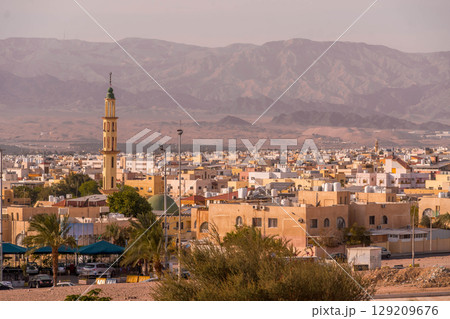 Panorama of Aqaba, a large Jordanian port city on the Red Sea, with a mosque minaret and colorful buildings set against the Israeli mountains at sunset. Panorama of Aqaba, a large Jordanian port city on the Red Sea, with a mosque minaret and colorful buildings set against the Israeli mountains at sunset. 129209676