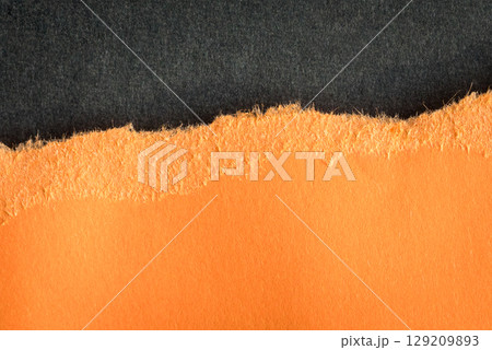 Torn orange paper with rough edges on top of dark gray color paper. Torn orange paper with rough edges on top of dark gray color paper. 129209893