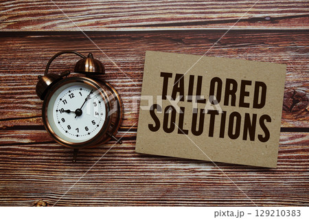 Tailored Solutions text with alarm clock on wooden background 129210383