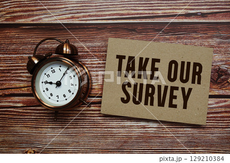 Take Our Survey text with alarm clock on wooden background Take Our Survey text with alarm clock on wooden background 129210384