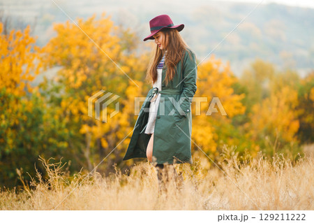 Beautiful stylish girl walks in the autumn park. The girl is dressed in a green coat and a red hat. 129211222