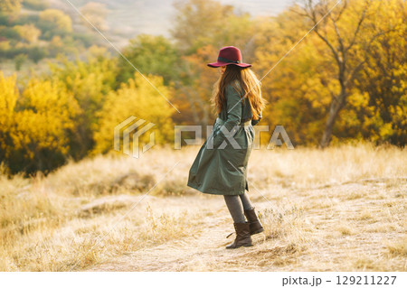 Beautiful stylish girl walks in the autumn park. The girl is dressed in a green coat and a red hat. Beautiful stylish girl walks in the autumn park. The girl is dressed in a green coat and a red hat. 129211227