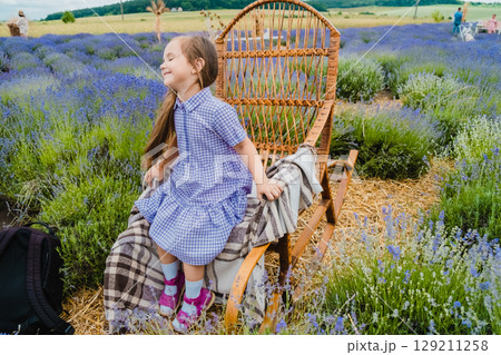 A girl with long, loose hair and a purple dress is sitting in a rocking chair in a lavender field A girl with long, loose hair and a purple dress is sitting in a rocking chair in a lavender field 129211258