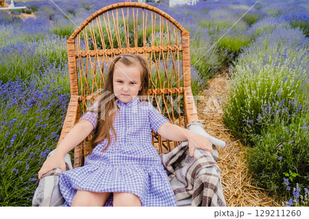 The delicate purple shade of the girl's dress echoes the color of the lavender among which she is sitting in the rocking chair 129211260