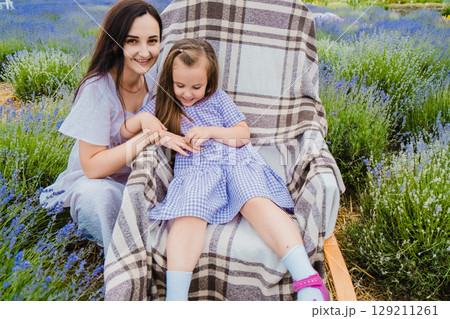 A girl sits in a rocking chair among lavender next to her mother 129211261