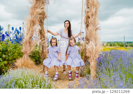 In the middle of a gentle lavender field stands a swing on which a young mother swings her two daughters 129211269