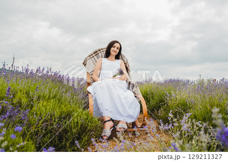 A girl in a white dress sits on a rocking chair in the middle of a lavender field 129211327