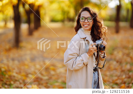 Woman taking pictures in autumn forest. Smiling woman enjoying autumn weather. Lifestyle concept. 129211516