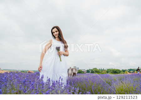 A beautiful woman in a long white dress stands in the middle of a lavender field A beautiful woman in a long white dress stands in the middle of a lavender field 129211523