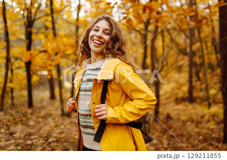 Hiking in autumn forest. Smiling tourist in bright coat walks through autumn park in sunny weather. 129211855