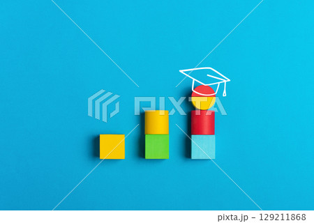 Graduation and education concept with colorful blocks and academic cap on a blue background. Symbol of learning, growth, and academic achievement Graduation and education concept with colorful blocks and academic cap on a blue background. Symbol of learning, growth, and academic achievement 129211868