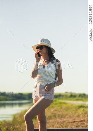 A young lady in light summer clothes stands by the lake A young lady in light summer clothes stands by the lake 129211994