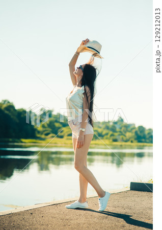 A young woman wearing a hat, shorts and a T-shirt raises her headdress above her as if dancing with the air 129212013