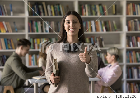 Excited student girl showing thumbs up to camera in classroom 129212220