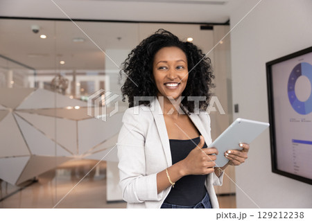 Smiling businesswoman looking aside distracted from using tablet in office Smiling businesswoman looking aside distracted from using tablet in office 129212238