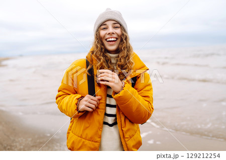 A beautiful young tourist woman in a yellow jacket with a backpack enjoys life near the sea. Travel. A beautiful young tourist woman in a yellow jacket with a backpack enjoys life near the sea. Travel. 129212254