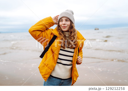 A beautiful young tourist woman in a yellow jacket with a backpack enjoys life near the sea. Travel. A beautiful young tourist woman in a yellow jacket with a backpack enjoys life near the sea. Travel. 129212258