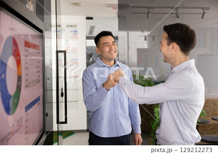 Two businessmen exchanging friendly fist bump in modern office Two businessmen exchanging friendly fist bump in modern office 129212273