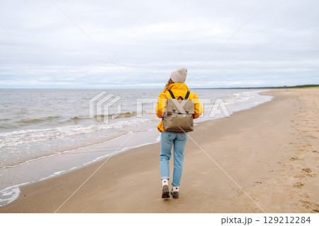 Attractive woman on windy cold beach. Beautiful tourist woman in stylish clothes enjoys life by sea. Attractive woman on windy cold beach. Beautiful tourist woman in stylish clothes enjoys life by sea. 129212284