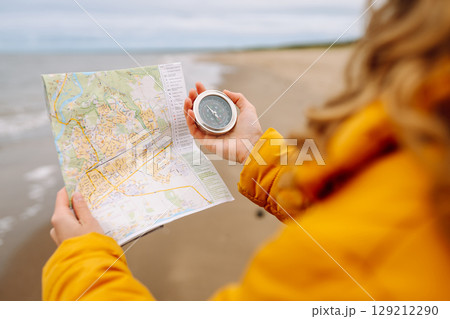 Traveler explorer young woman holding compass, map in hands on beach near the sea. Active lifestyle. 129212290