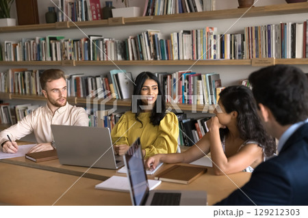 Group of professionals sit at table with laptops and notepads Group of professionals sit at table with laptops and notepads 129212303
