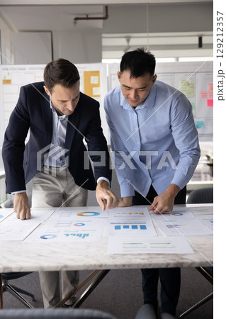Colleagues deeply engaged in analyzing printed financial and statistical charts 129212357