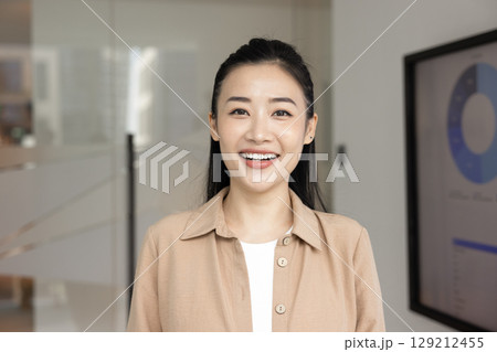 Headshot portrait cheerful millennial businesswoman looking at camera in office Headshot portrait cheerful millennial businesswoman looking at camera in office 129212455